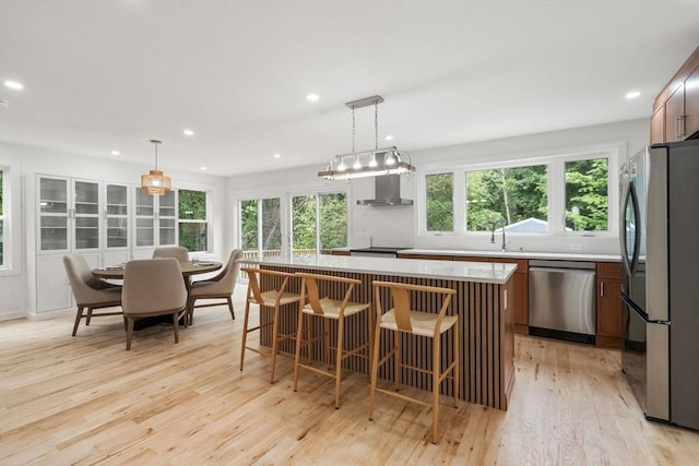 174 Gilbert St, Mansfield, MA 02048 - kitchen with stainless steel appliances, light wood finished floors, a kitchen island, light countertops, and wall chimney exhaust hood