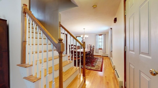 staircase with a notable chandelier, a baseboard heating unit, and wood-type flooring