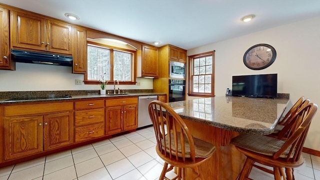 kitchen featuring sink, light tile patterned floors, a kitchen bar, dark stone countertops, and black appliances