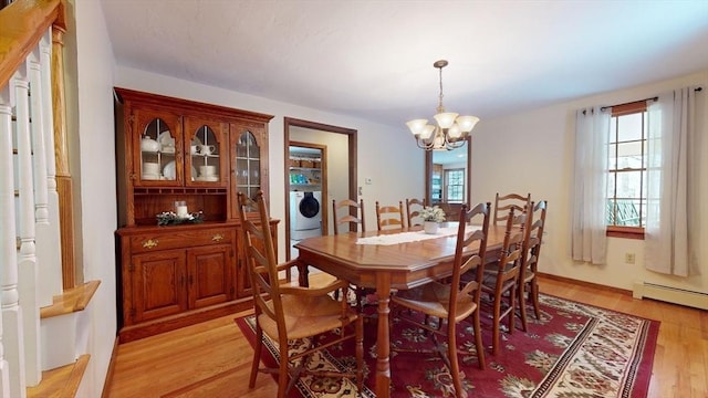 dining room with baseboard heating, washer / clothes dryer, light wood-type flooring, plenty of natural light, and a chandelier