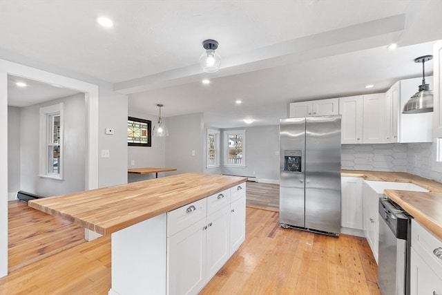 kitchen with appliances with stainless steel finishes, pendant lighting, white cabinetry, and butcher block counters