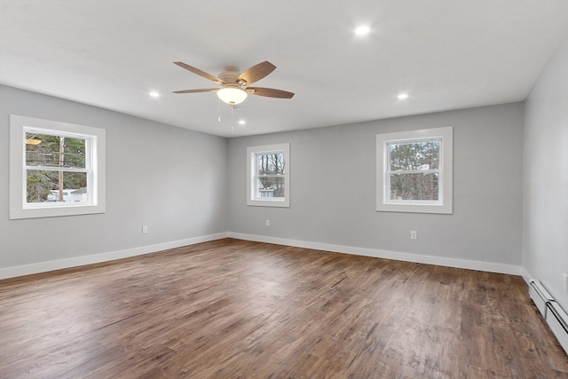 empty room with a wealth of natural light, ceiling fan, a baseboard heating unit, and dark hardwood / wood-style floors