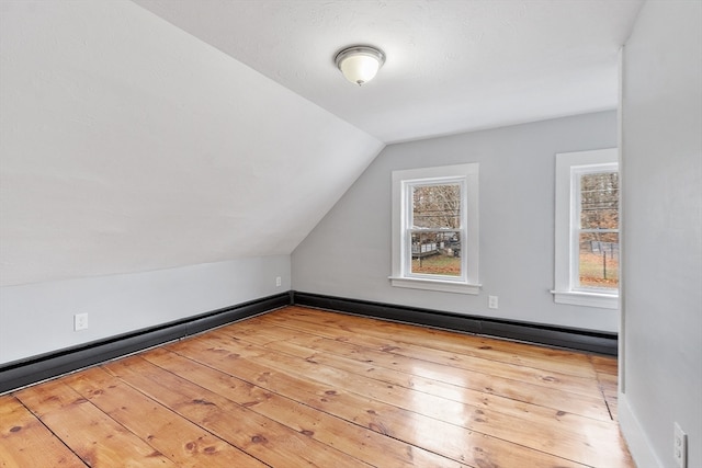 additional living space with vaulted ceiling, a baseboard heating unit, and light hardwood / wood-style floors