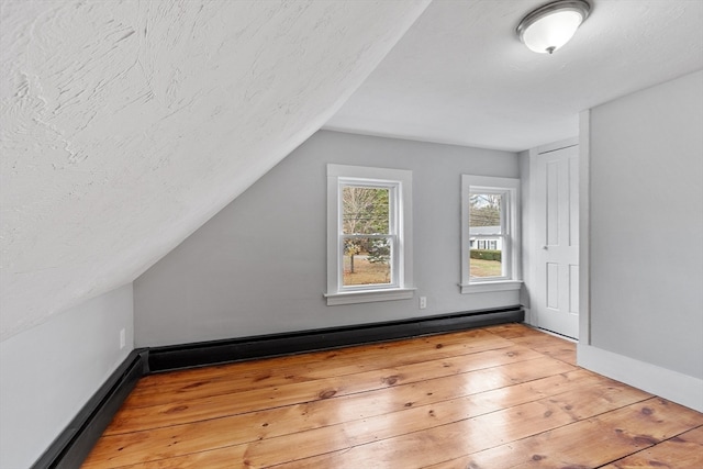 bonus room featuring light hardwood / wood-style flooring, a baseboard radiator, lofted ceiling, and a textured ceiling