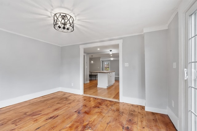 empty room with ornamental molding, a chandelier, a healthy amount of sunlight, and light hardwood / wood-style floors