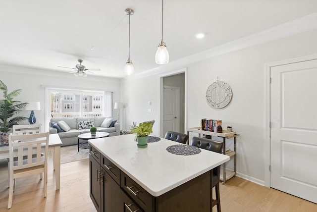 kitchen featuring ceiling fan, a breakfast bar, light wood finished floors, a kitchen island, and ornamental molding