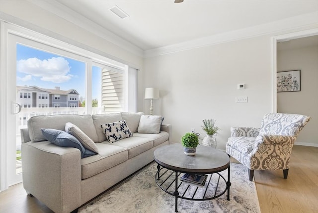living room featuring crown molding, baseboards, visible vents, and light wood-style flooring