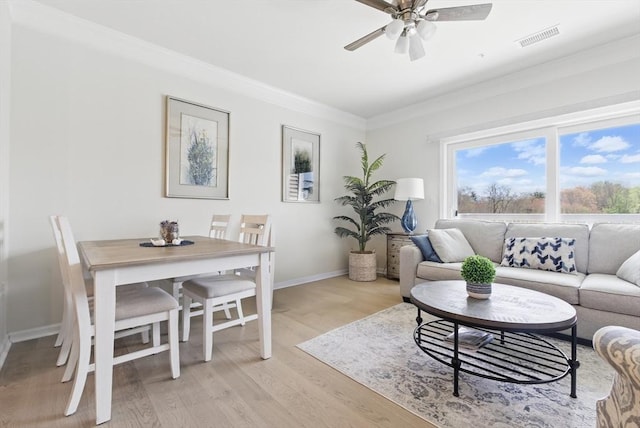 living room featuring crown molding, light wood finished floors, a ceiling fan, baseboards, and visible vents