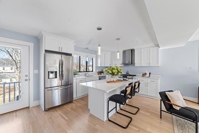 kitchen with stainless steel appliances, light countertops, wall chimney range hood, and white cabinetry