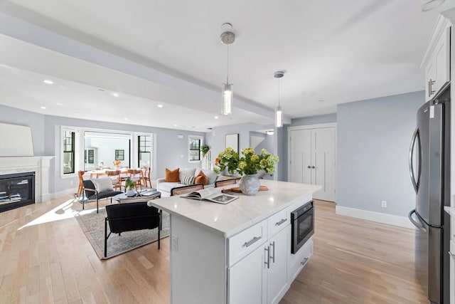 kitchen with black microwave, a high end fireplace, open floor plan, light wood-type flooring, and freestanding refrigerator