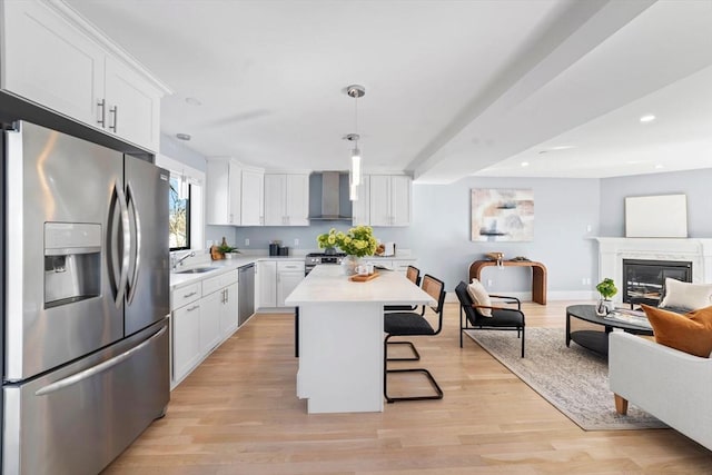 kitchen with a kitchen bar, light countertops, appliances with stainless steel finishes, open floor plan, and wall chimney exhaust hood