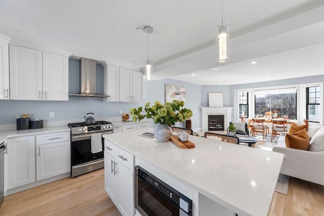 kitchen with appliances with stainless steel finishes, open floor plan, light wood-style flooring, and wall chimney exhaust hood