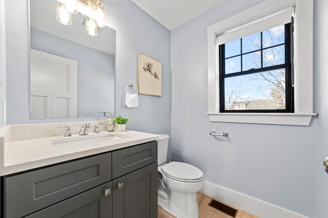 half bathroom with baseboards, visible vents, toilet, wood finished floors, and vanity