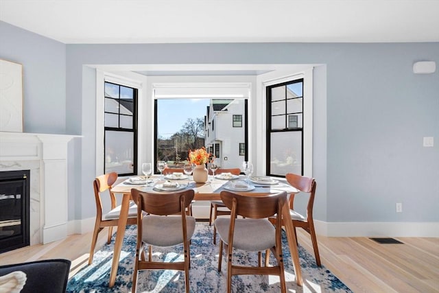 dining area featuring visible vents, light wood finished floors, a high end fireplace, and baseboards