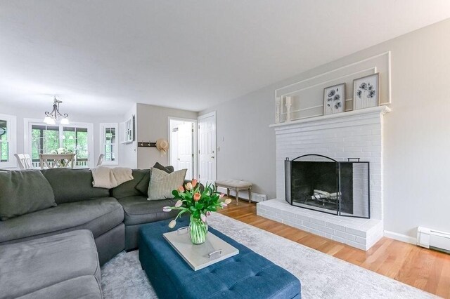 living area featuring wood finished floors, a chandelier, a brick fireplace, and baseboard heating