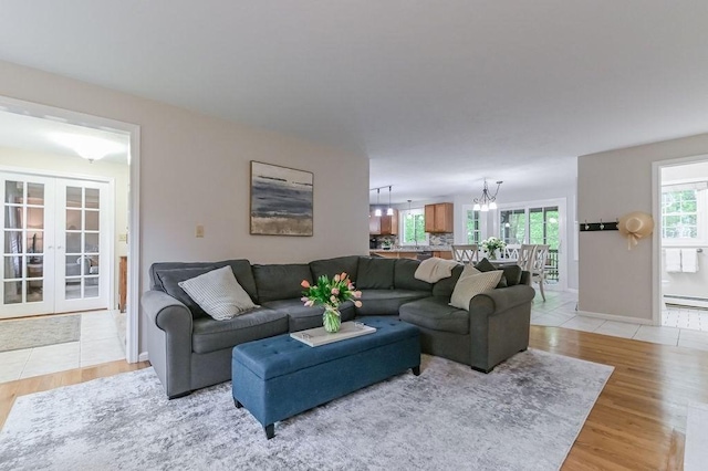 living area with french doors, a baseboard radiator, a chandelier, light wood-type flooring, and baseboards
