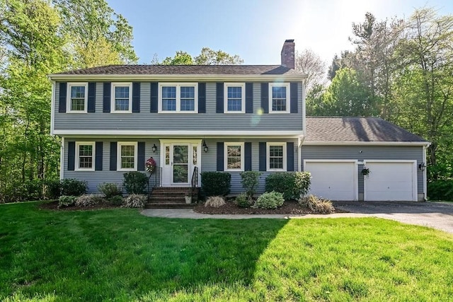 colonial inspired home with a chimney, an attached garage, asphalt driveway, and a front yard