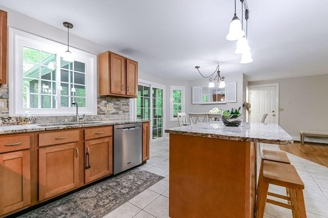 kitchen with stainless steel dishwasher, brown cabinetry, tasteful backsplash, and a chandelier
