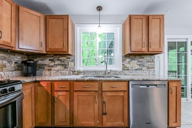 kitchen featuring appliances with stainless steel finishes, a sink, light stone counters, decorative backsplash, and brown cabinets