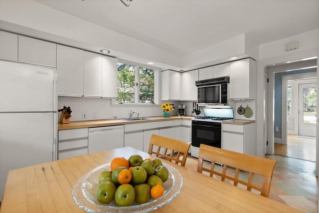 kitchen with white appliances, white cabinetry, plenty of natural light, and a sink