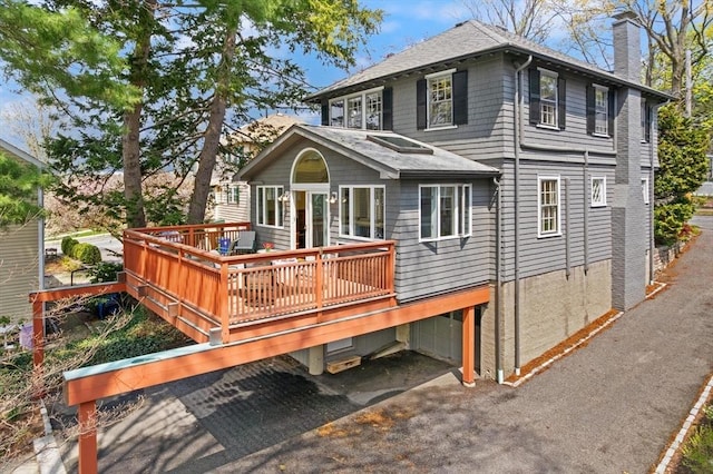 back of property featuring a deck, a chimney, and roof with shingles