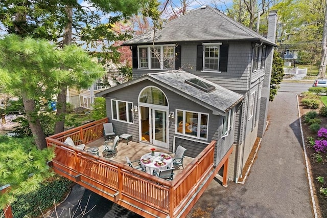 rear view of property with roof with shingles, outdoor dining area, a wooden deck, and a chimney