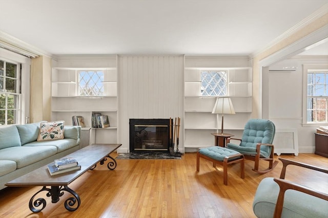living room featuring ornamental molding, built in shelves, hardwood / wood-style flooring, and a fireplace