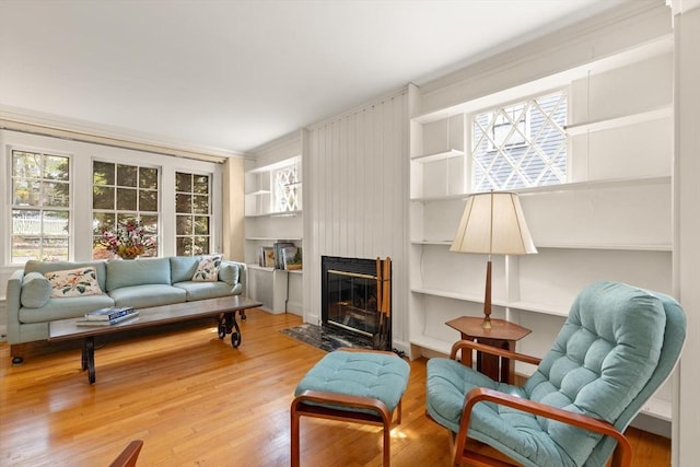 living room featuring a fireplace with flush hearth, built in features, crown molding, and wood finished floors