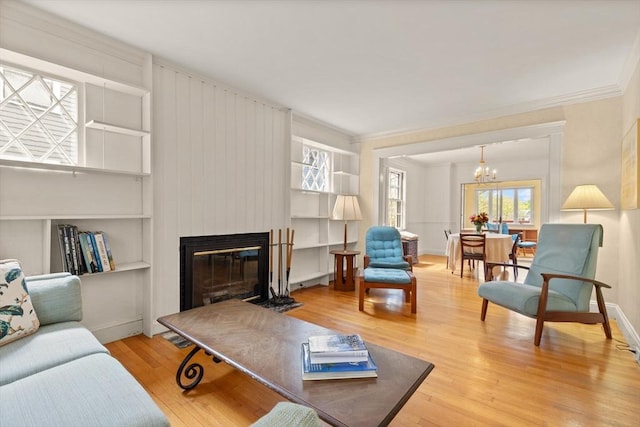 living room featuring a chandelier, a glass covered fireplace, built in shelves, baseboards, and wood finished floors