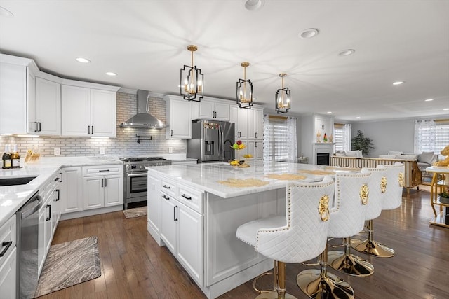 kitchen featuring a kitchen island, dark wood finished floors, white cabinets, appliances with stainless steel finishes, and wall chimney range hood