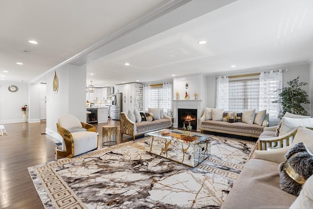 living room with crown molding, baseboards, a lit fireplace, recessed lighting, and wood finished floors