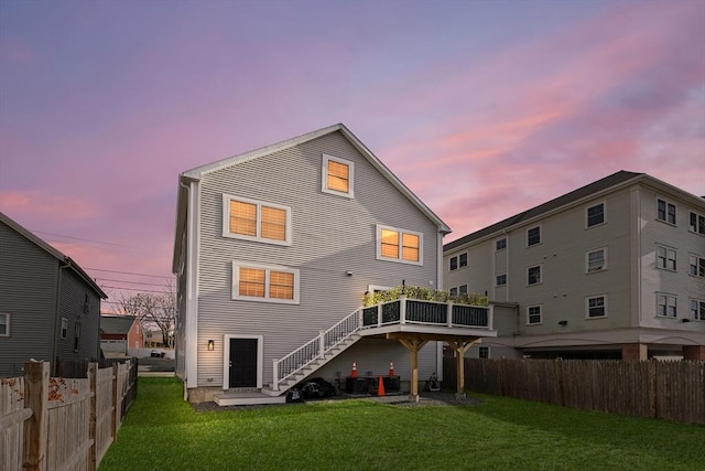 back of house at dusk featuring a lawn, stairs, and fence