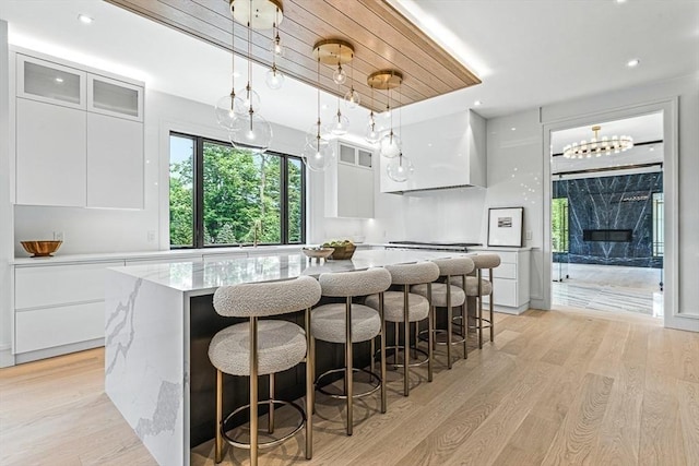 kitchen featuring light wood finished floors, a spacious island, glass insert cabinets, white cabinetry, and modern cabinets