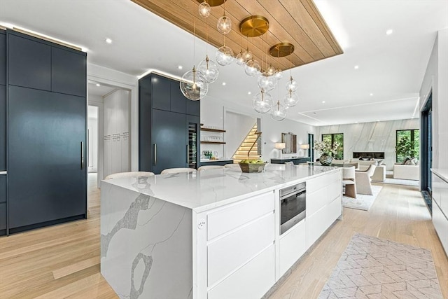 kitchen featuring light stone counters, light wood finished floors, hanging light fixtures, modern cabinets, and a large island with sink