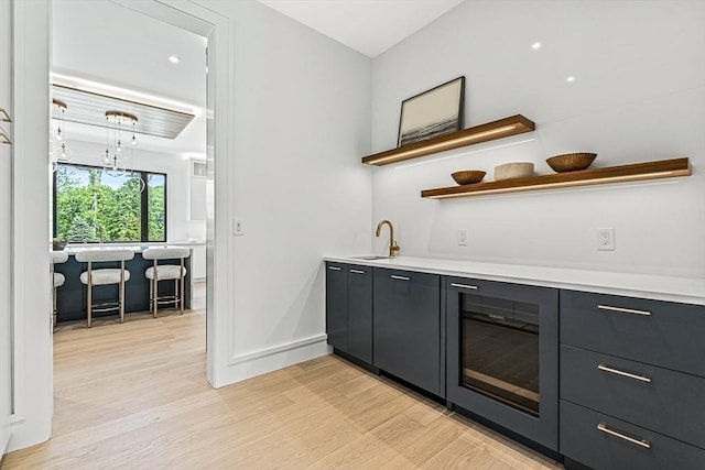 bar featuring light wood-style floors, wet bar, baseboards, and a sink