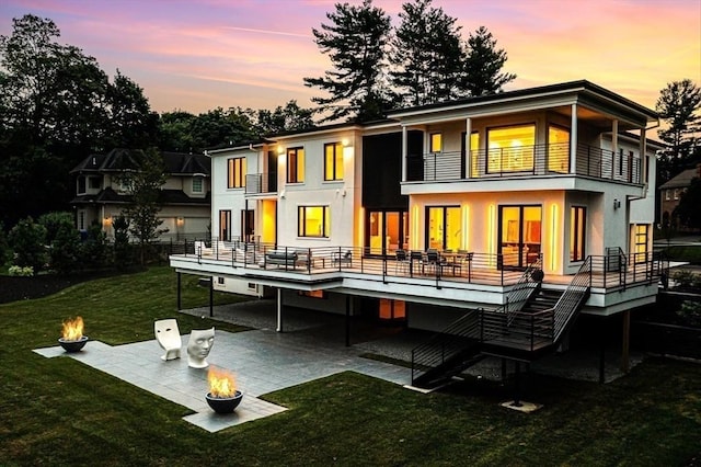 rear view of house featuring a lawn, a balcony, stairway, a patio area, and stucco siding