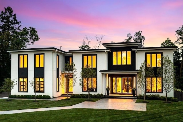 back of house at dusk featuring entry steps, a yard, and stucco siding