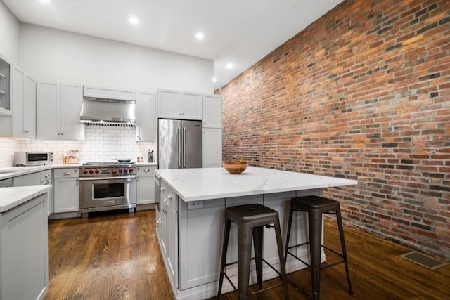 kitchen with brick wall, a breakfast bar, premium appliances, exhaust hood, and a kitchen island