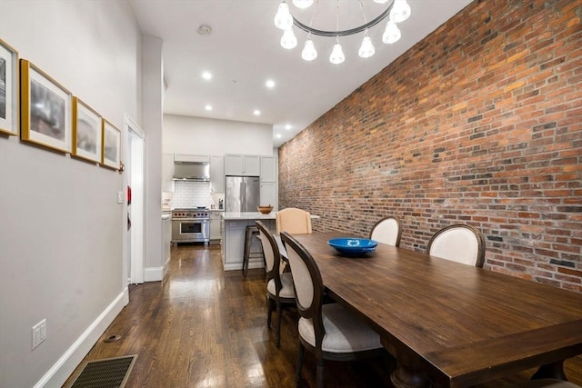 dining space featuring a towering ceiling, dark wood-type flooring, brick wall, and a chandelier