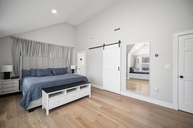 bedroom featuring light wood-type flooring, a barn door, and high vaulted ceiling