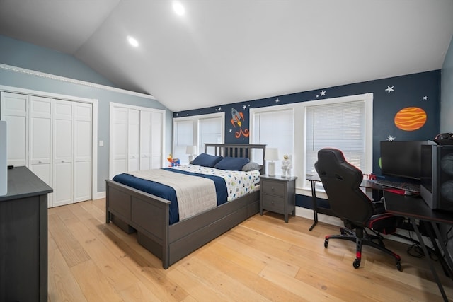 bedroom with light hardwood / wood-style flooring, lofted ceiling, and multiple closets