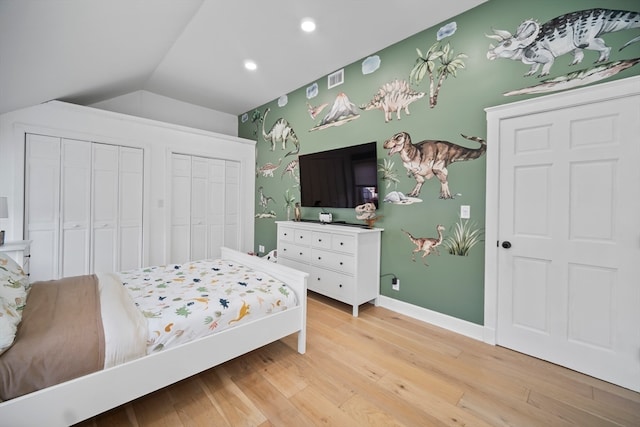 bedroom with lofted ceiling, light hardwood / wood-style flooring, and two closets