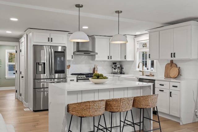 kitchen featuring white cabinets, appliances with stainless steel finishes, a kitchen island, and wall chimney exhaust hood