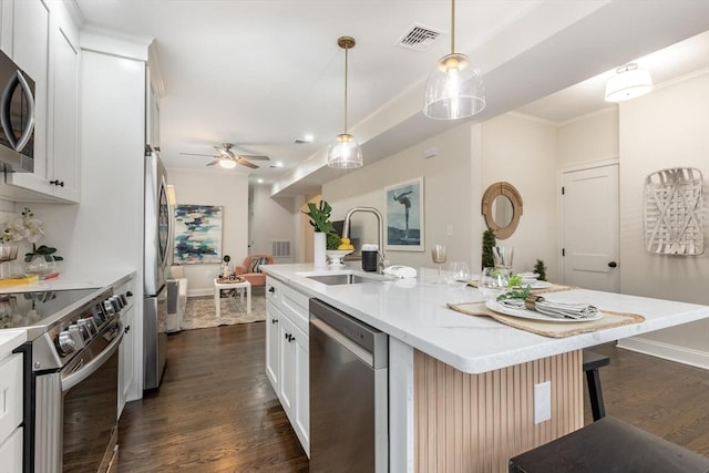 kitchen with a kitchen island with sink, a sink, a ceiling fan, appliances with stainless steel finishes, and dark wood finished floors