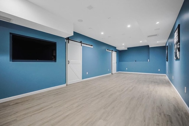 empty room featuring a barn door, wood finished floors, baseboards, and recessed lighting