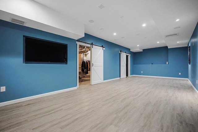 unfurnished living room with a barn door, wood finished floors, baseboards, and recessed lighting