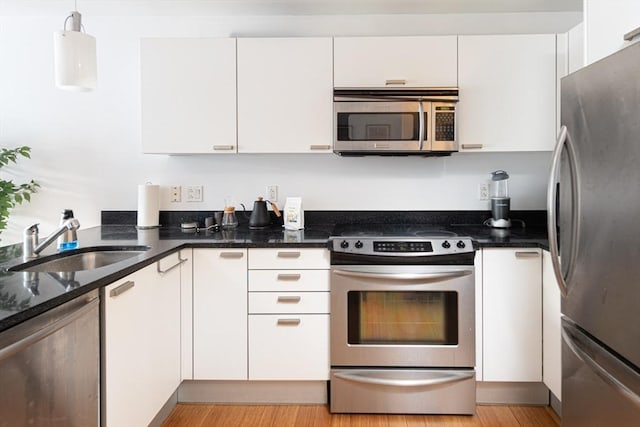 kitchen featuring sink, white cabinetry, dark stone countertops, appliances with stainless steel finishes, and pendant lighting