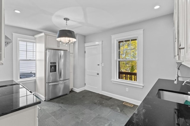 kitchen featuring stainless steel refrigerator with ice dispenser, white cabinets, baseboards, and a wealth of natural light