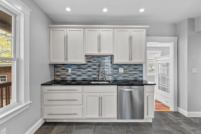 kitchen featuring stainless steel dishwasher, dark countertops, decorative backsplash, and a sink