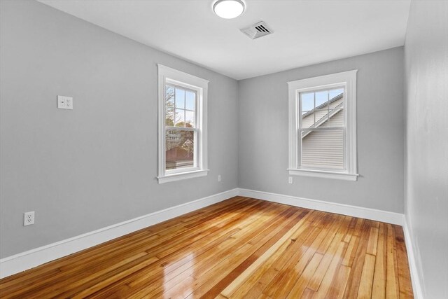 empty room with visible vents, wood-type flooring, plenty of natural light, and baseboards